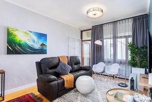 Un soggiorno moderno con un divano in pelle, un pouf bianco rotondo, un quadro di grandi dimensioni e vista panoramica attraverso una porta in vetro.