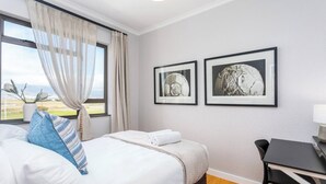 A hotel room with a bed, a desk, and two framed pictures on the wall. - Burmeister Circle by Ctha (Milnerton)