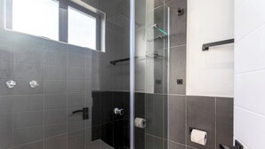 A modern bathroom with a glass-enclosed shower, dark tiles, and a window providing natural light. - Burmeister Circle by Ctha (Milnerton)