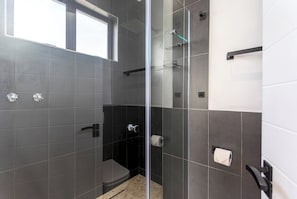 Un bagno moderno con cabina doccia in vetro, piastrelle scure e una finestra che offre luce naturale.