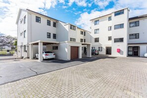 Un edificio residenziale a più piani con un'area parcheggio coperta e un vialetto lastricato.
