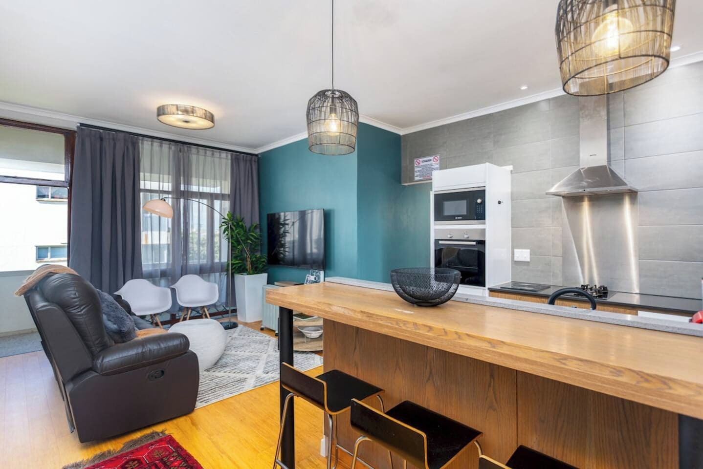 Una sala de estar moderna con sofá, un comedor con barra, una cocina con microondas y un ventanal grande.