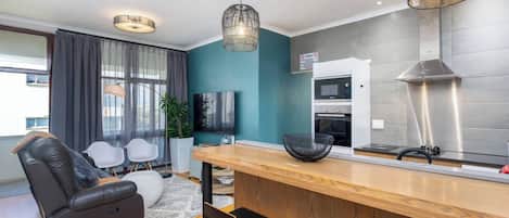 Una sala de estar moderna con sofá, un comedor con barra, una cocina con microondas y un ventanal grande.
