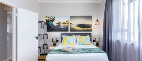 A modern bedroom with a bed, two bedside tables, a wardrobe, and artwork on the wall.