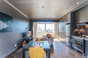 Una cucina moderna con elettrodomestici in acciaio inossidabile, una zona pranzo con tavolo e sedie e un soggiorno con divano e una grande finestra.