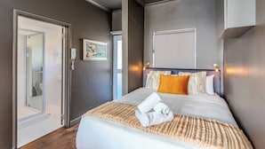 A hotel room with a bed, a painting, and a door leading to a bathroom. - Granada Court 309 by Ctha (Cape Town)