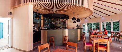 Un restaurante con mobiliario de madera, una zona de bar y grandes ventanales.