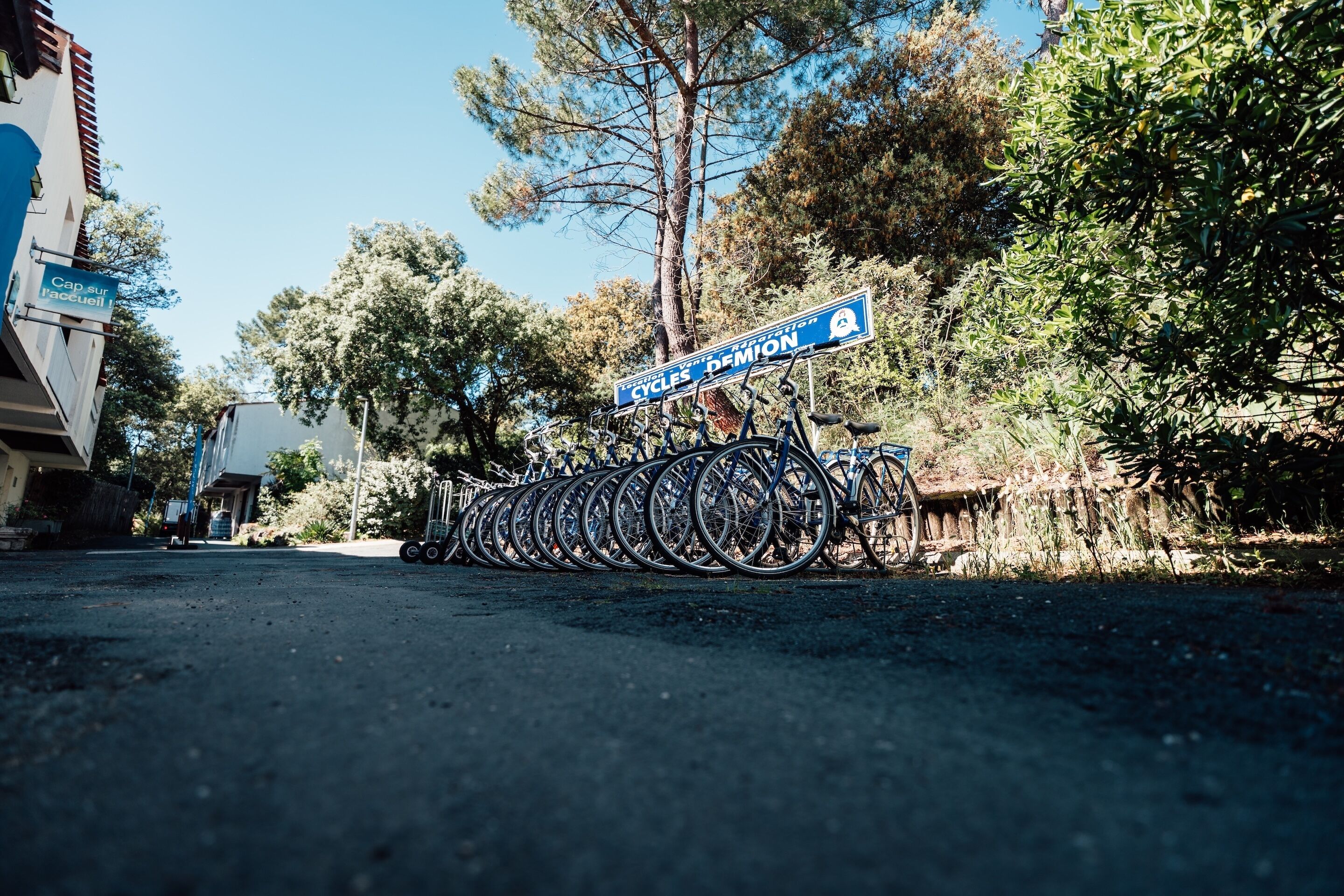 Una strada con un cartello per 'CYCLES DEMION' e un'area di parcheggio per biciclette.