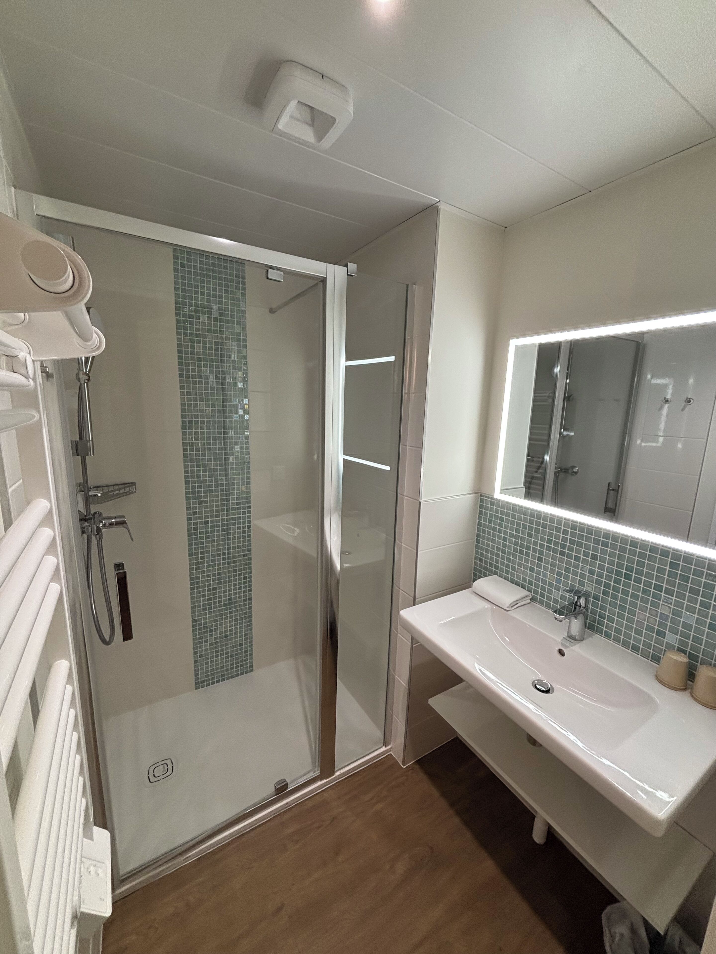 A bathroom with a glass shower enclosure, a white sink, and a mirror with a lighted frame.