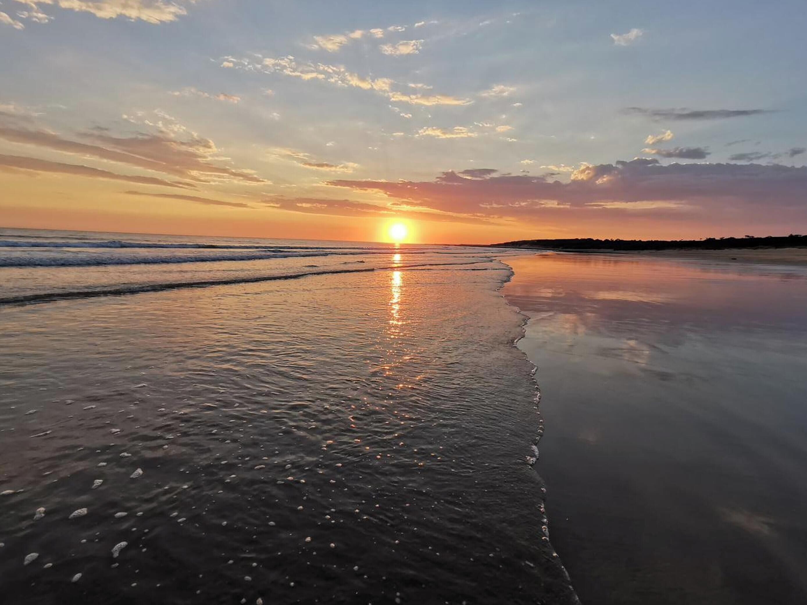 Een strand bij zonsondergang, met rustig water en een verre horizon.