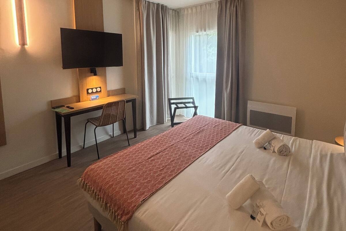 A hotel room with a bed, a desk with a TV, and a chair.