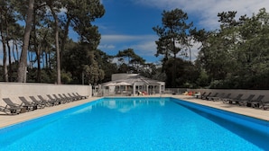 A swimming pool with lounge chairs, a covered seating area, and trees in the background. - Club Vacances Bleues Le Grand Air (Saint-Trojan-les-Bains)