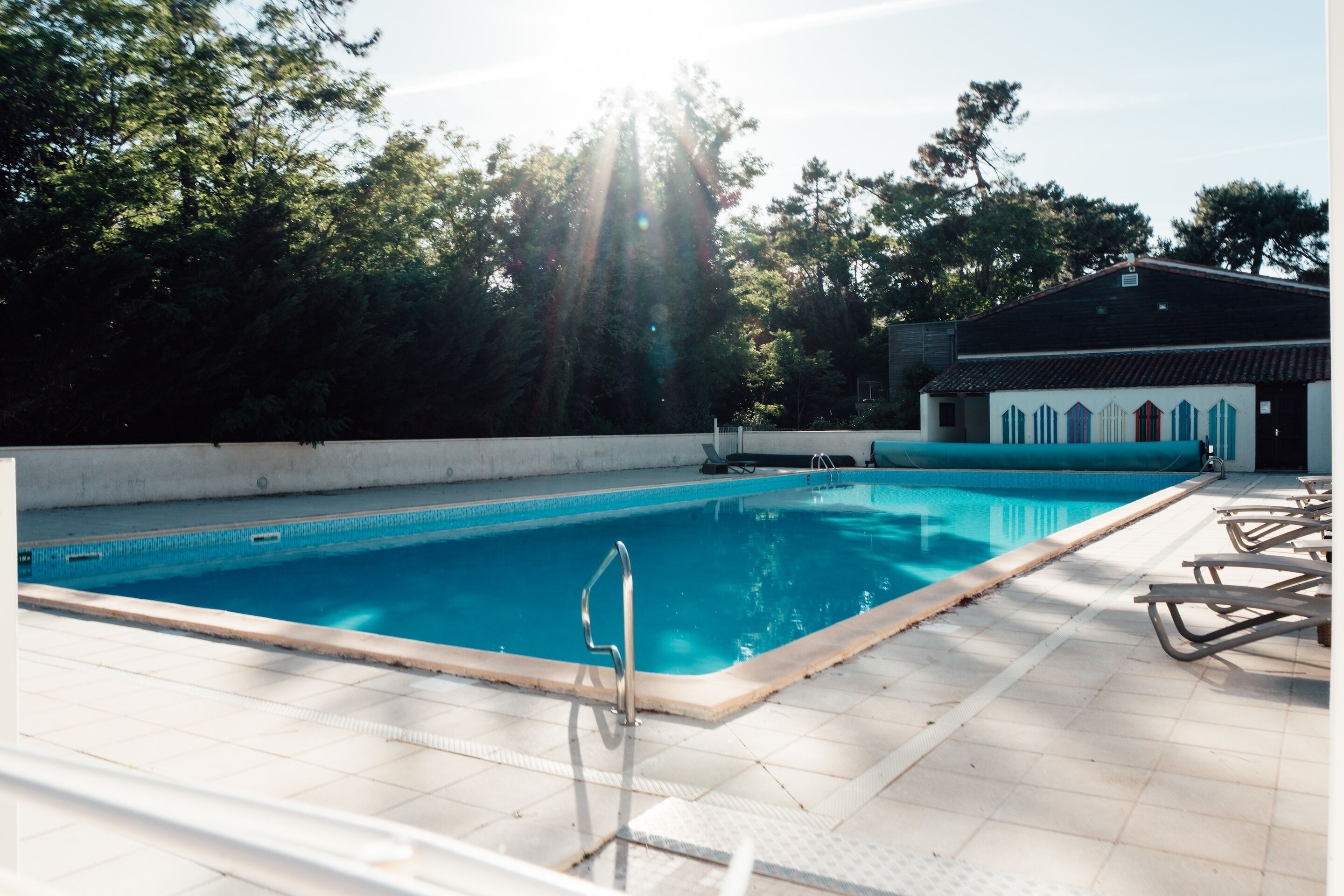 Une piscine avec une terrasse carrelée, un escalier en métal et des chaises longues.
