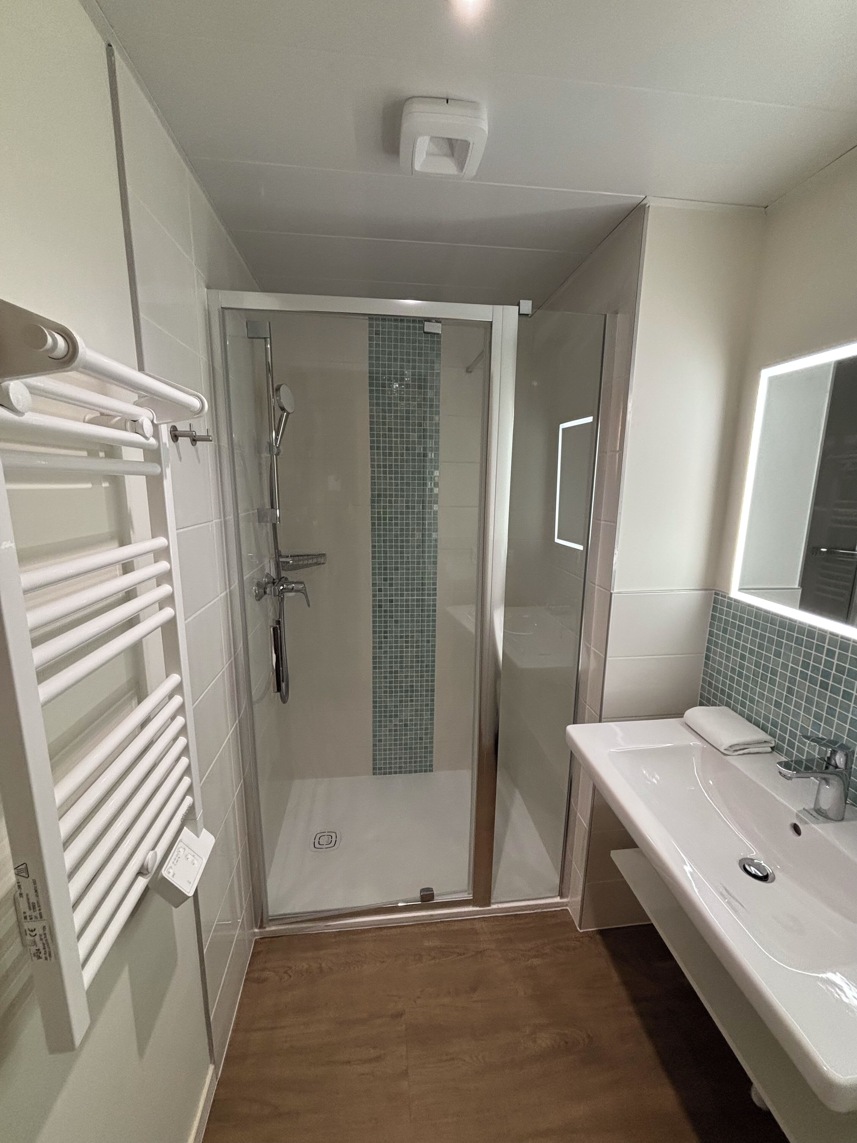 Een badkamer met een douche met glazen wand, een wit wastafelmeubel en een handdoekhouder.