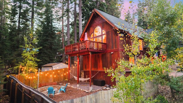 Un rustico chalet con un balcone, immerso tra alberi e dotato di un patio in legno con luci decorative.