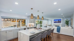 A modern kitchen with a marble island, pendant lighting, and a dining area with bar stools. - Modern SoCal Escape with Outdoor Grill & Lush Lounge Areas | Casa Cordero (Mission Viejo)