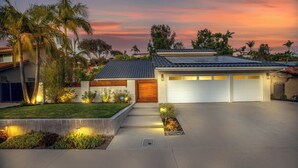 A modern house with a garage, a well-maintained lawn, and a sunset sky. - Modern SoCal Escape with Outdoor Grill & Lush Lounge Areas | Casa Cordero (Mission Viejo)