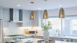 A modern kitchen with a central island, bar stools, pendant lighting, and a large window. - Modern SoCal Escape with Outdoor Grill & Lush Lounge Areas | Casa Cordero (Mission Viejo)