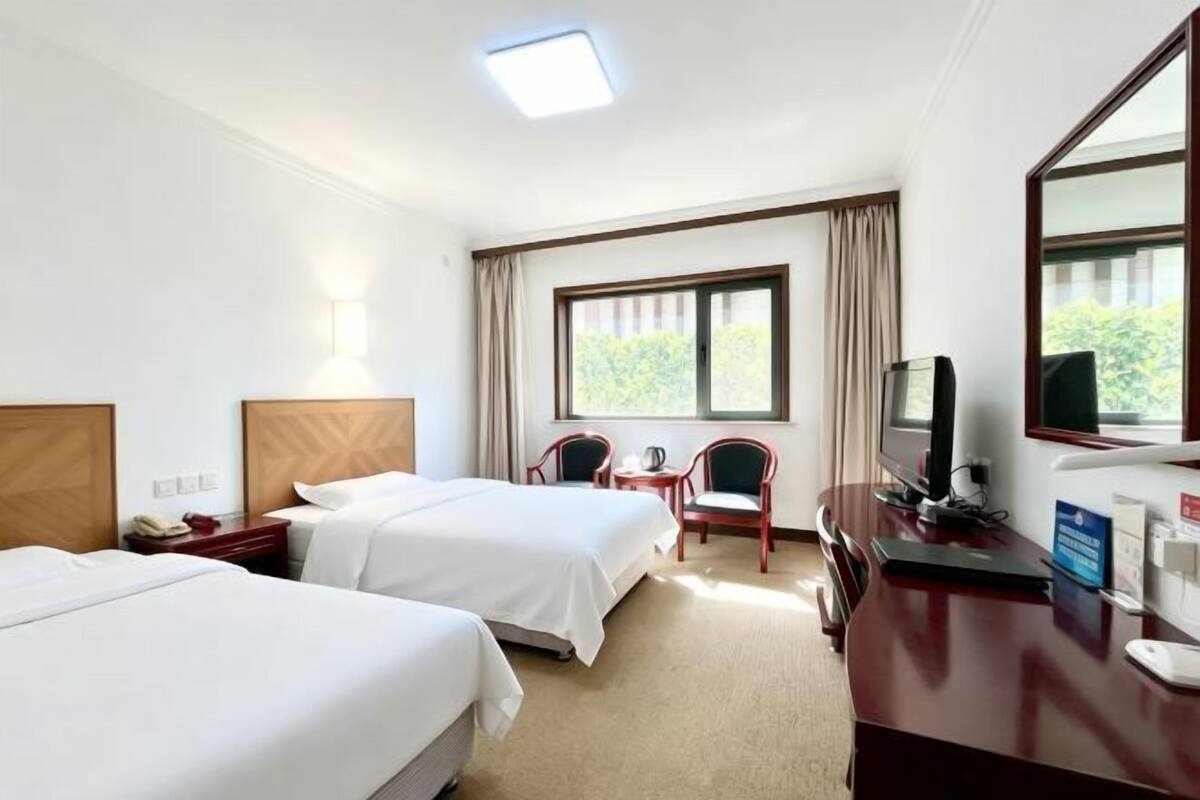 Une chambre d’hôtel avec deux lits, un bureau avec un ordinateur, une télévision et une fenêtre avec des rideaux.