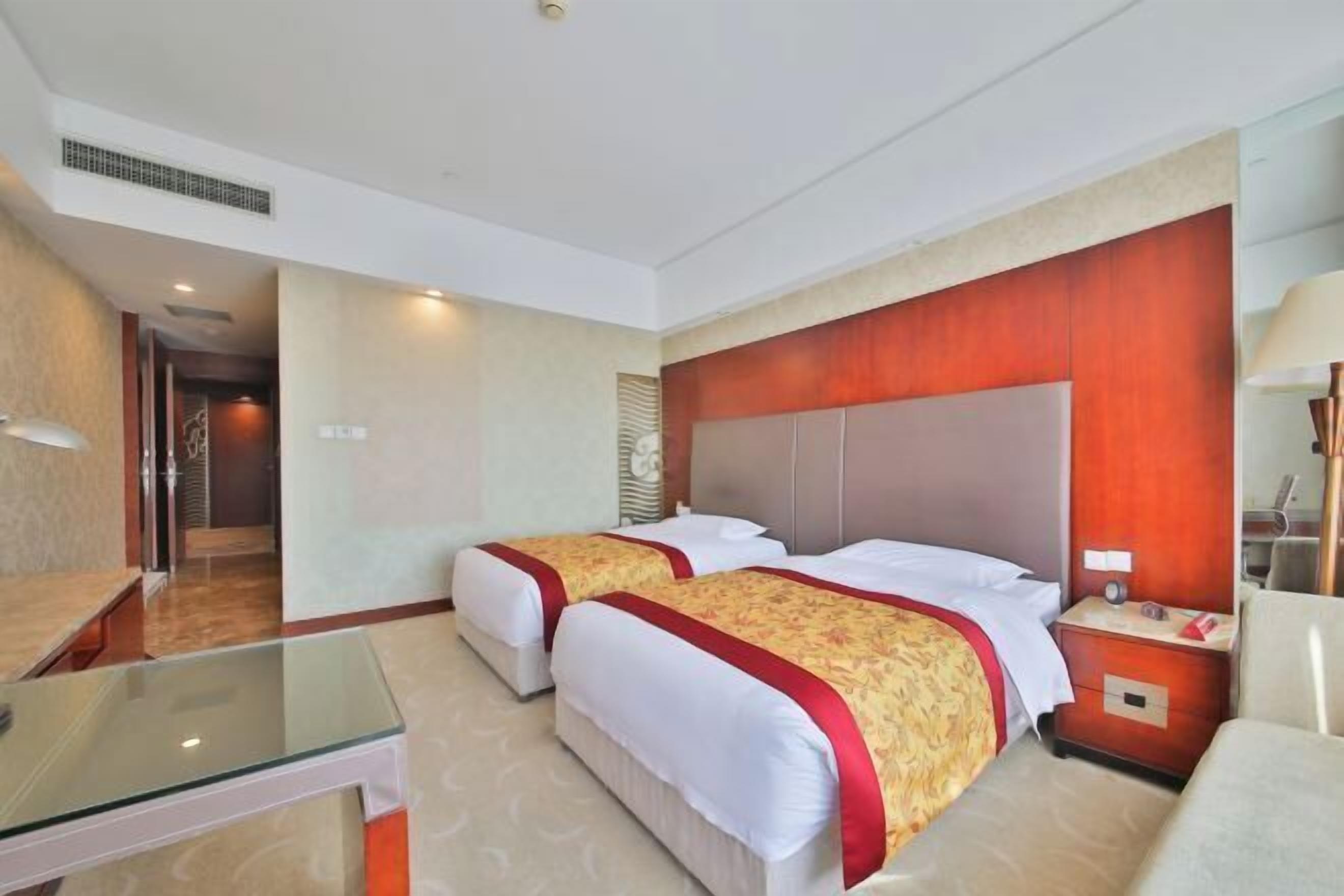 Quarto de hotel com duas camas, uma mesa de vidro, uma mesinha de cabeceira de madeira e um espelho.