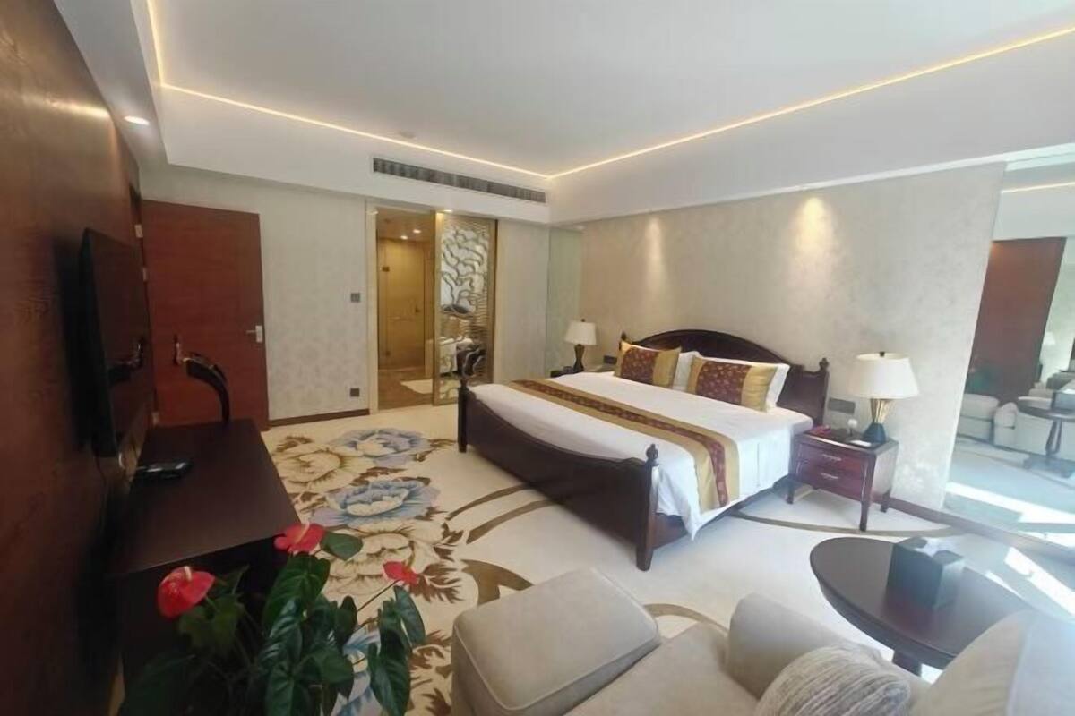 Une chambre d’hôtel comprenant un lit, des tables de chevet, un bureau, une télévision et un grand miroir.