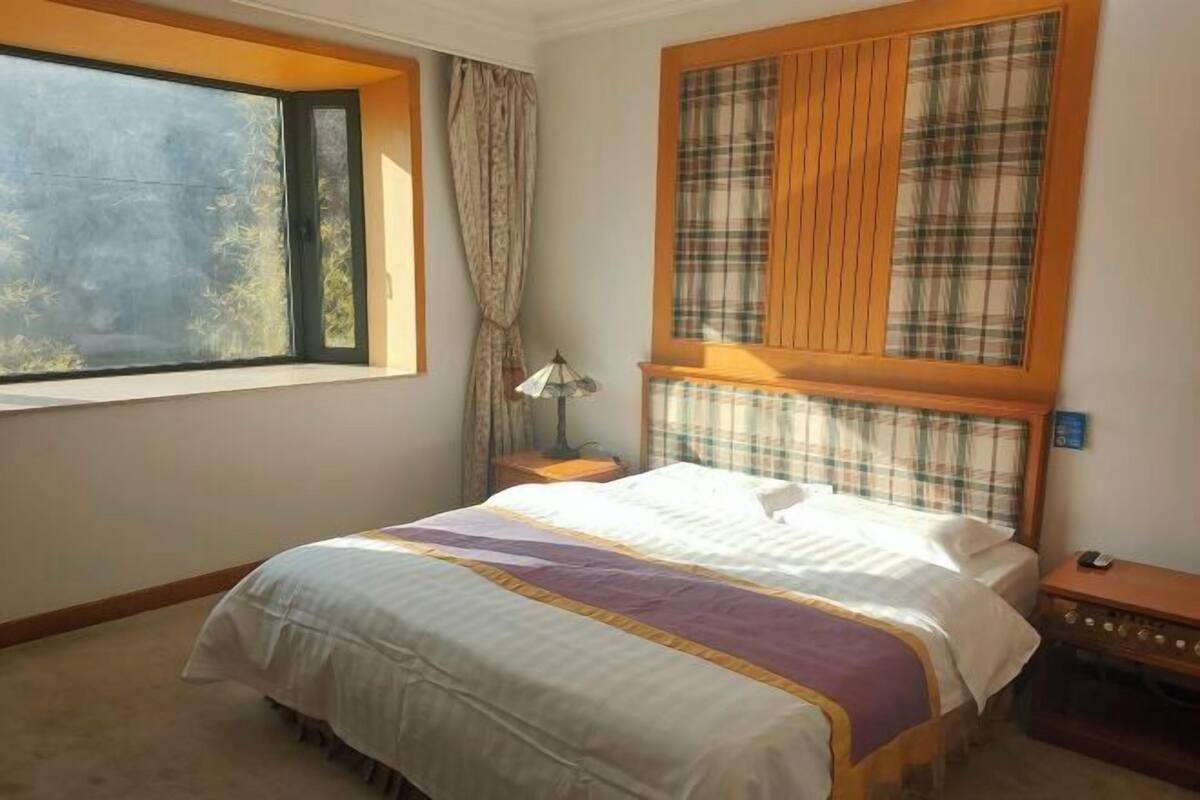 Une chambre avec une grande fenêtre, un lit recouvert d’une courtepointe à rayures, une table de chevet et une lampe.