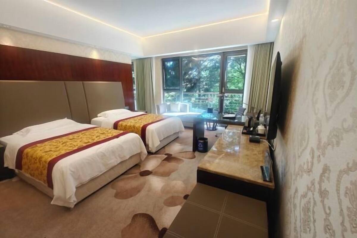 Une chambre d’hôtel avec deux lits, une petite table, un téléviseur et une vue sur l’extérieur.
