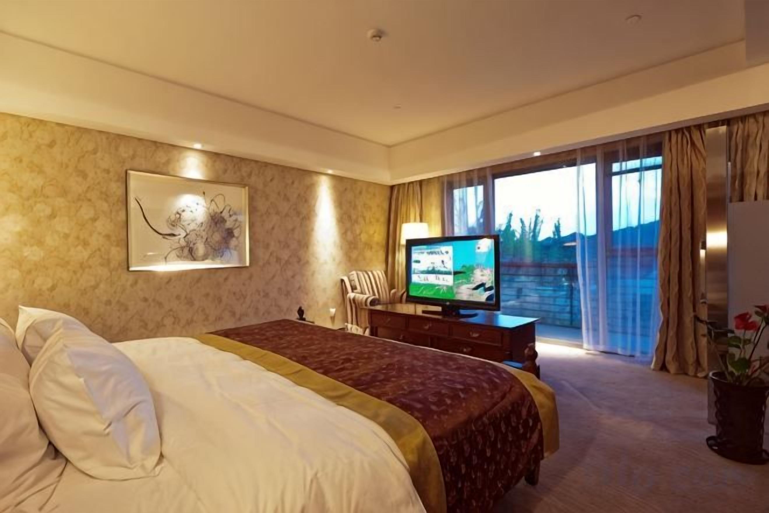A hotel room with a large bed, a television, a desk, and a view of the outdoors.