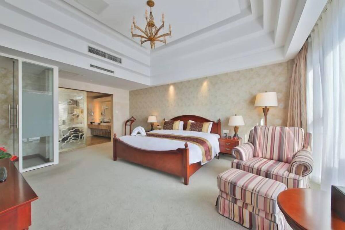 Une chambre d’hôtel avec un lit, une chaise, un bureau, une lampe et un lustre.