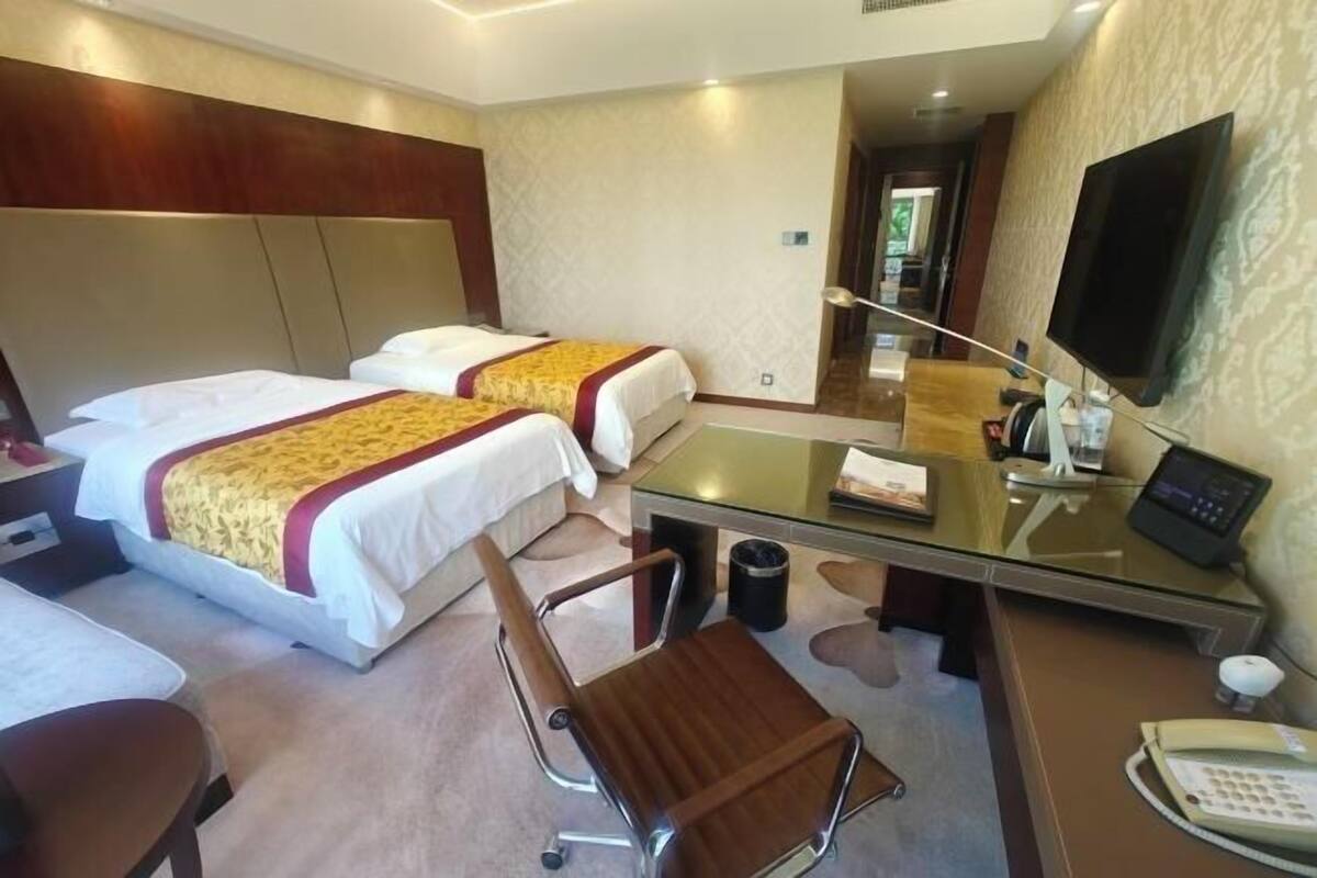 Une chambre d’hôtel avec deux lits, un bureau avec un téléphone, une chaise et un téléviseur.