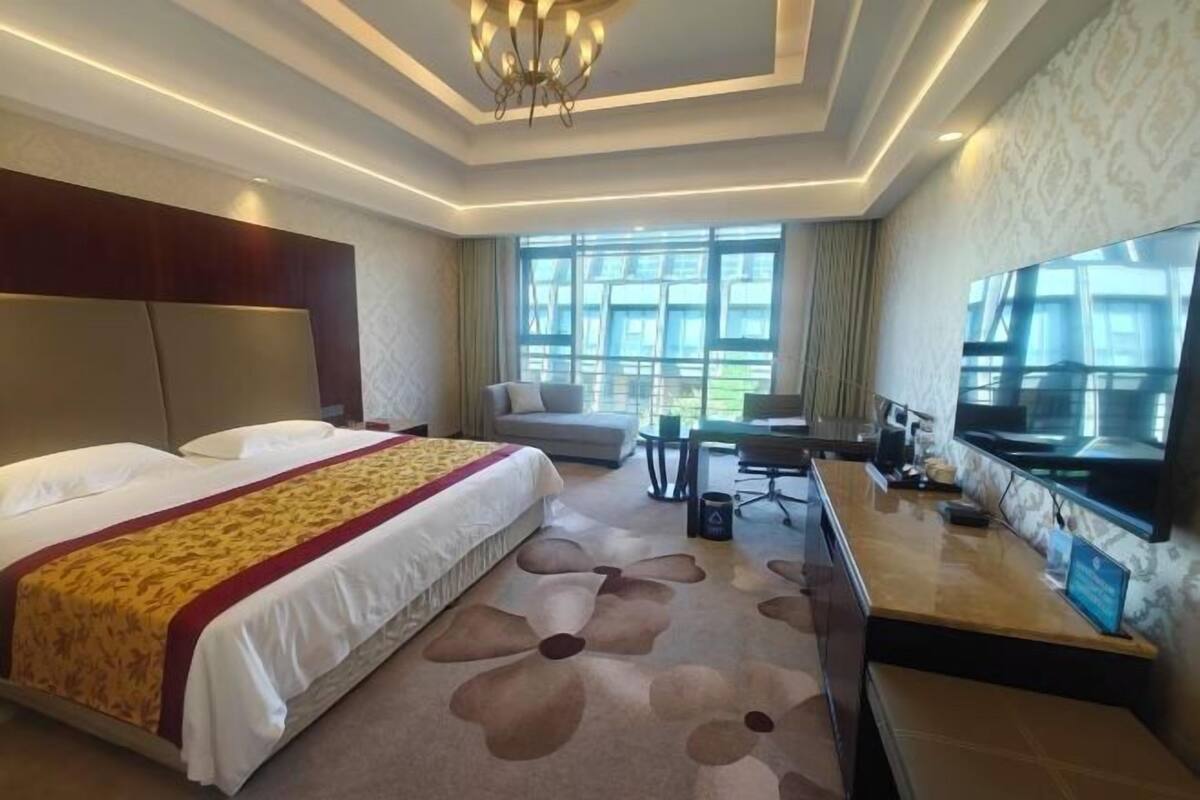 Une chambre d’hôtel avec un grand lit, un bureau avec une télévision et une vue sur l’extérieur par la fenêtre.