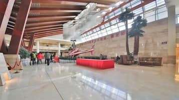 A spacious lobby with a high ceiling, a central red seating area, and a large window allowing natural light.