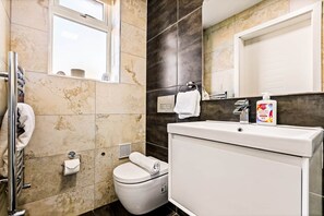 Een moderne badkamer met toilet, wastafel en douche. Handdoekrek met handdoeken, fles handzeep en spiegel boven de wastafel.