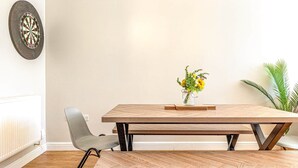 A dining area with a wooden table, a bench, a chair, a vase with flowers, and a dartboard on the wall. - Spacious & Modern 4-Bed Home – Sleeps 7 (Newquay)