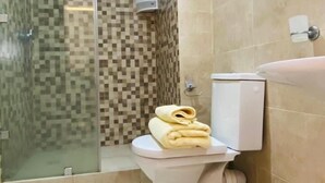 Et badeværelse med glasvæg omkring brusenichen, et toilet med et håndklæde ovenpå og fliserede vægge.