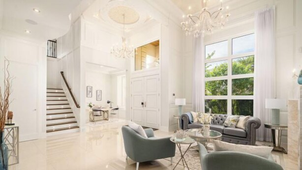 A spacious living area with a staircase, a grey sofa set, and a chandelier.