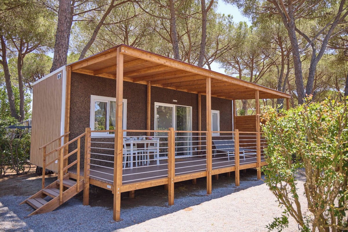 Eine Holzhütte mit einer überdachten Terrasse, einer kleinen Sitzgelegenheit im Freien und einem Kiesgrundstück.