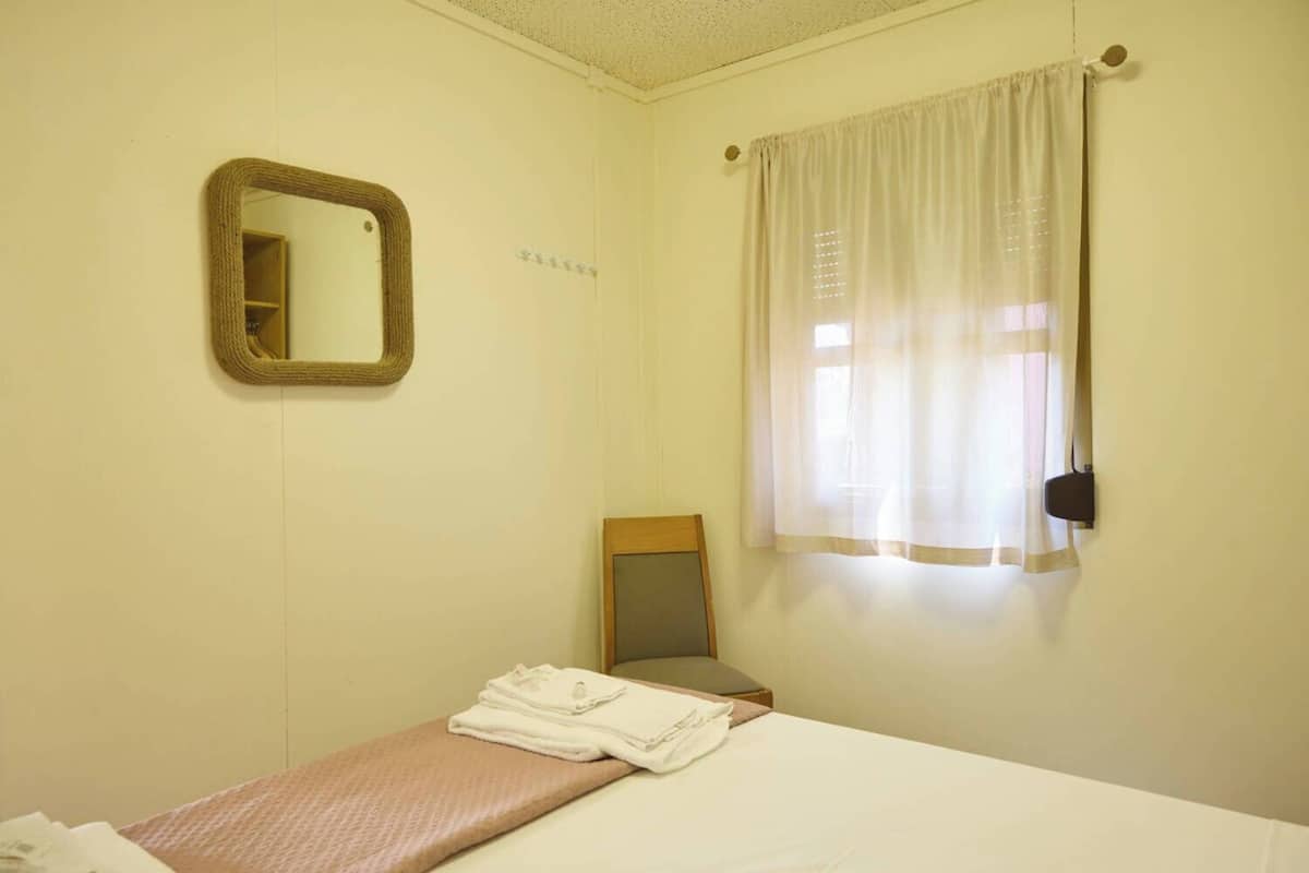 Ein schlichter Raum mit einem Bett, einem Spiegel und einem Fenster mit Vorhängen.
