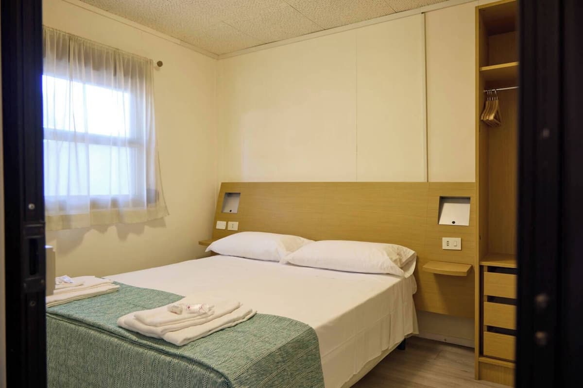 Ein Hotelzimmer mit einem Einzelbett, einem Holzkopfende, einem Nachttisch und einem Kleiderschrank.
