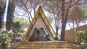 Una estructura de madera triangular con un dosel blanco, rodeada de árboles y una terraza de madera.