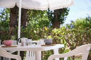 Mesa blanca al aire libre con un toldo, rodeada de follaje.