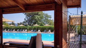 Zona de piscina con sillones de descanso y sombrillas, rodeada de follaje y un cielo despejado.