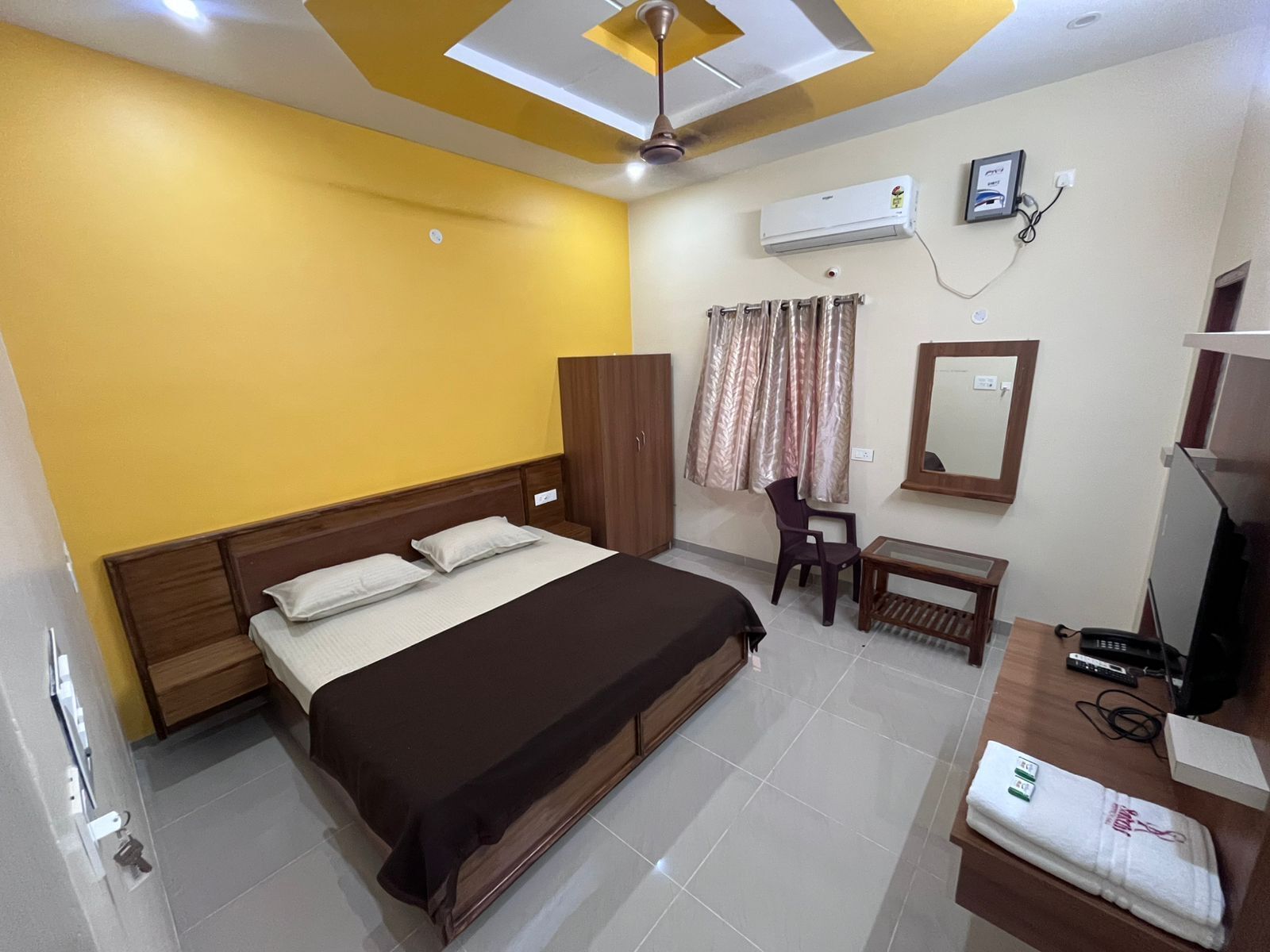 A hotel room with a bed, a desk, a chair, an air conditioning unit, and a television.