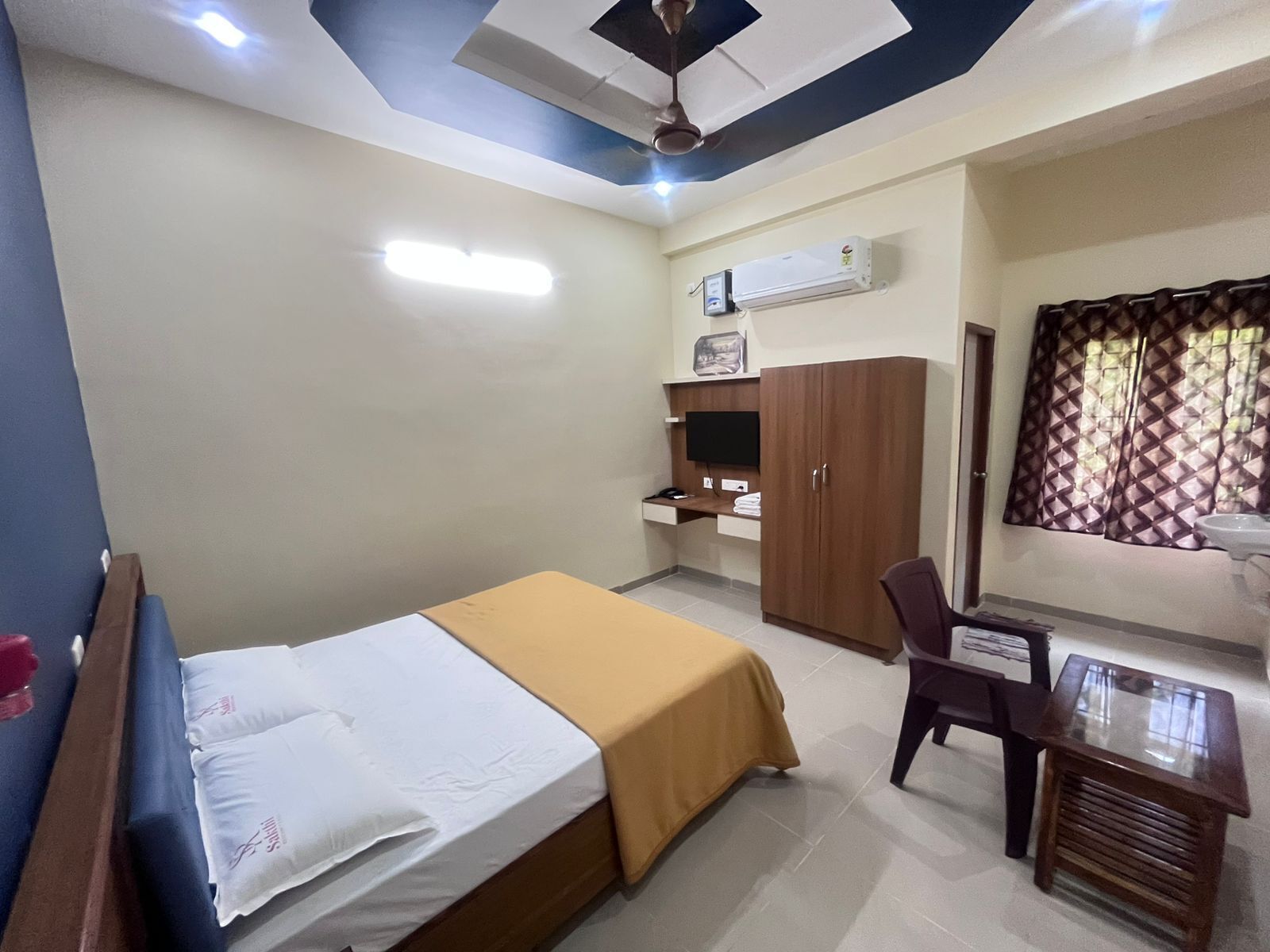 A bedroom with a bed, a desk, a wardrobe, and an air conditioning unit.