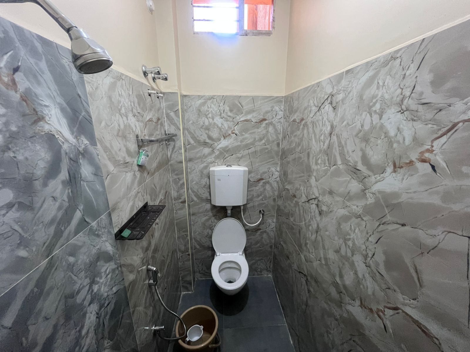 A bathroom with a toilet, a shower, and a marble wall.
