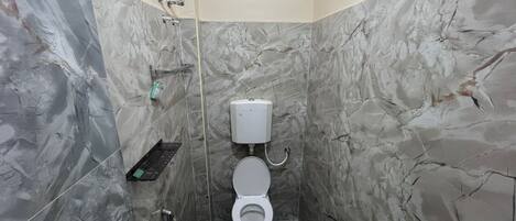 A bathroom with a toilet, a shower, and a marble wall.