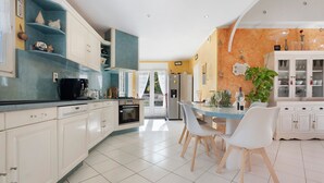 Een moderne keuken met witte kasten, een eethoek met witte stoelen en een grote potplant.