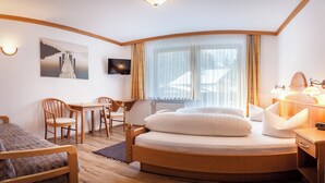 Een kleine hotelkamer met een rond bed, een bureau, een stoel, een televisie en een groot raam met gordijnen.