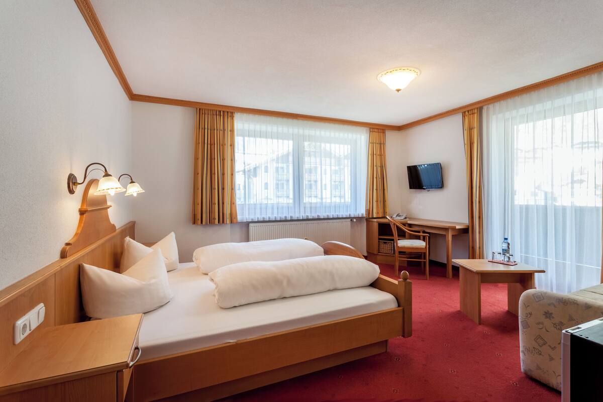 A hotel room with a bed, a desk, a chair, a TV, and a window with curtains.