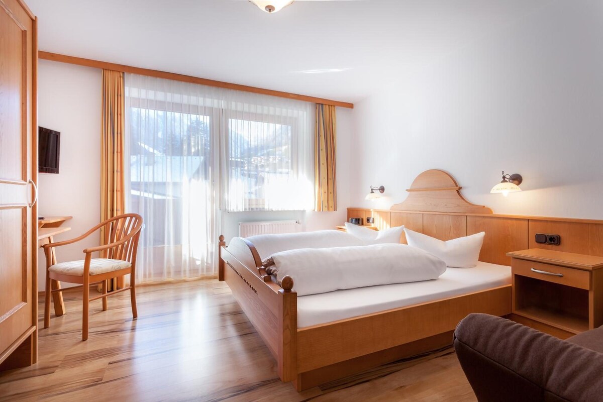 Una habitación de hotel con una cama de madera, una silla, un escritorio y una ventana con cortinas.